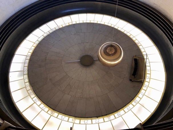 A large pendulum swings above a circular platform with marked numbers around its circumference. The setting appears to be indoors, with a focus on the pendulum's central movement and surrounding numbered markers.