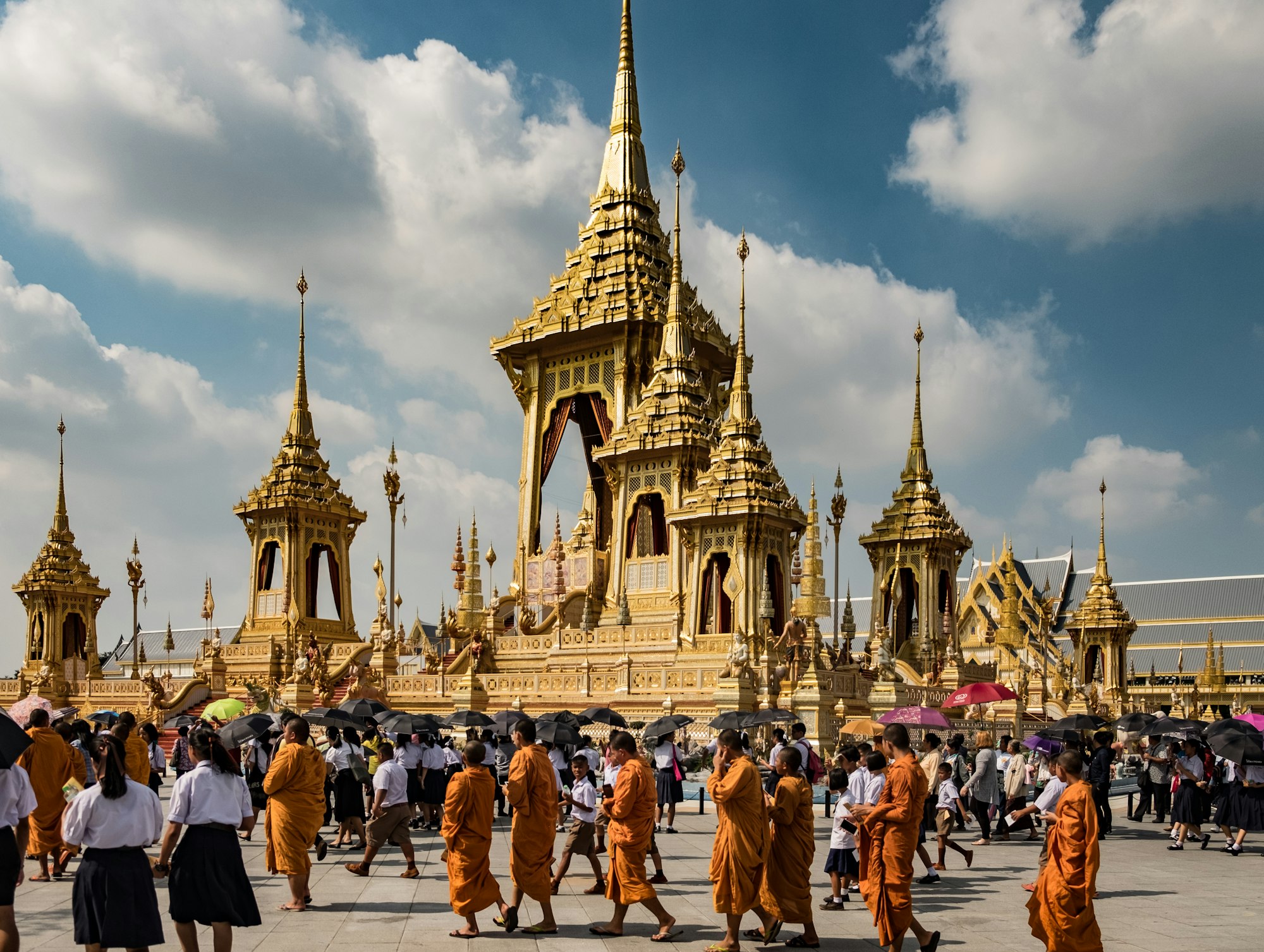 A group of monks walk around the Grand Palace in Bangkok during the mid-day sun.
