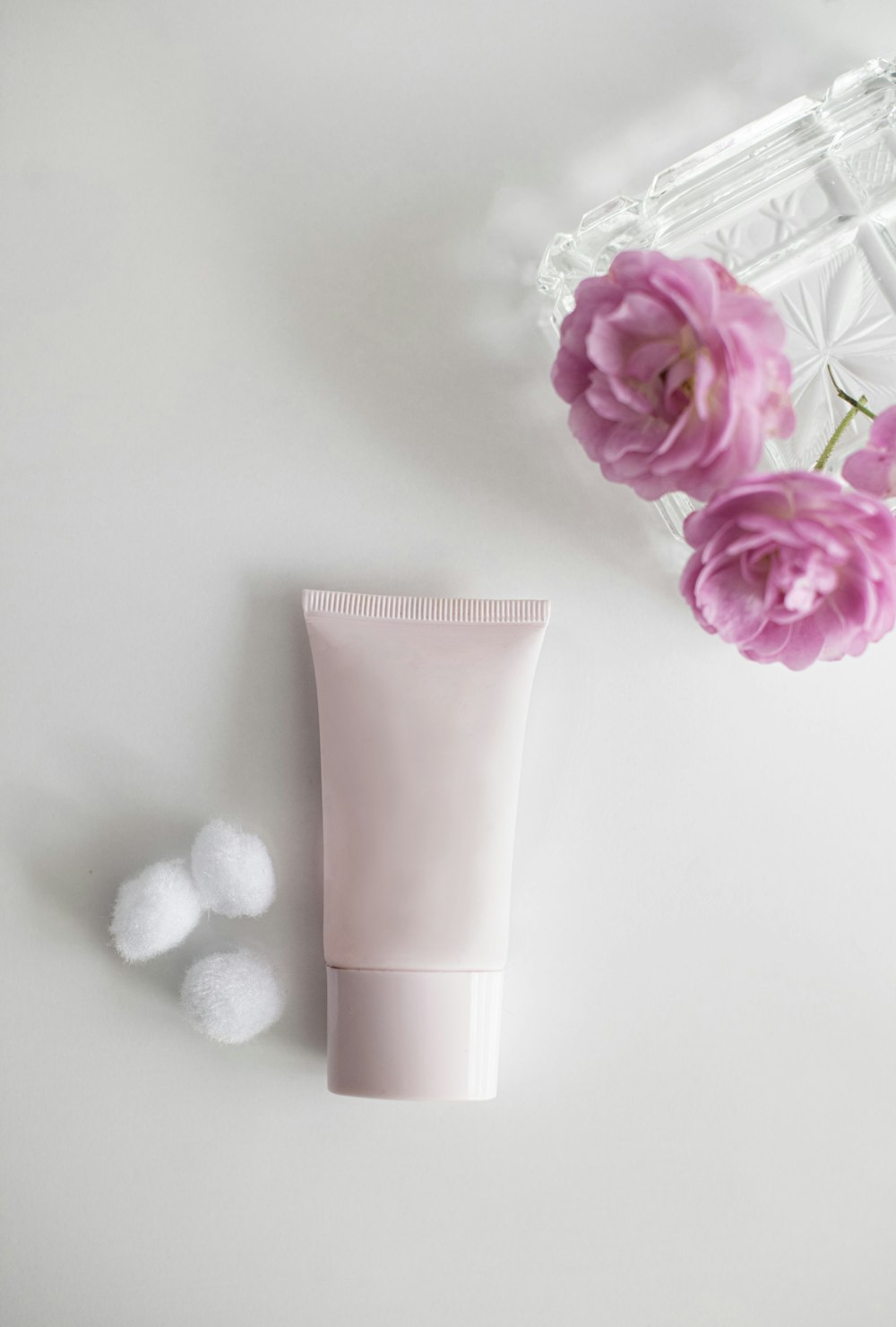Un tubo de crema junto a una flor rosa