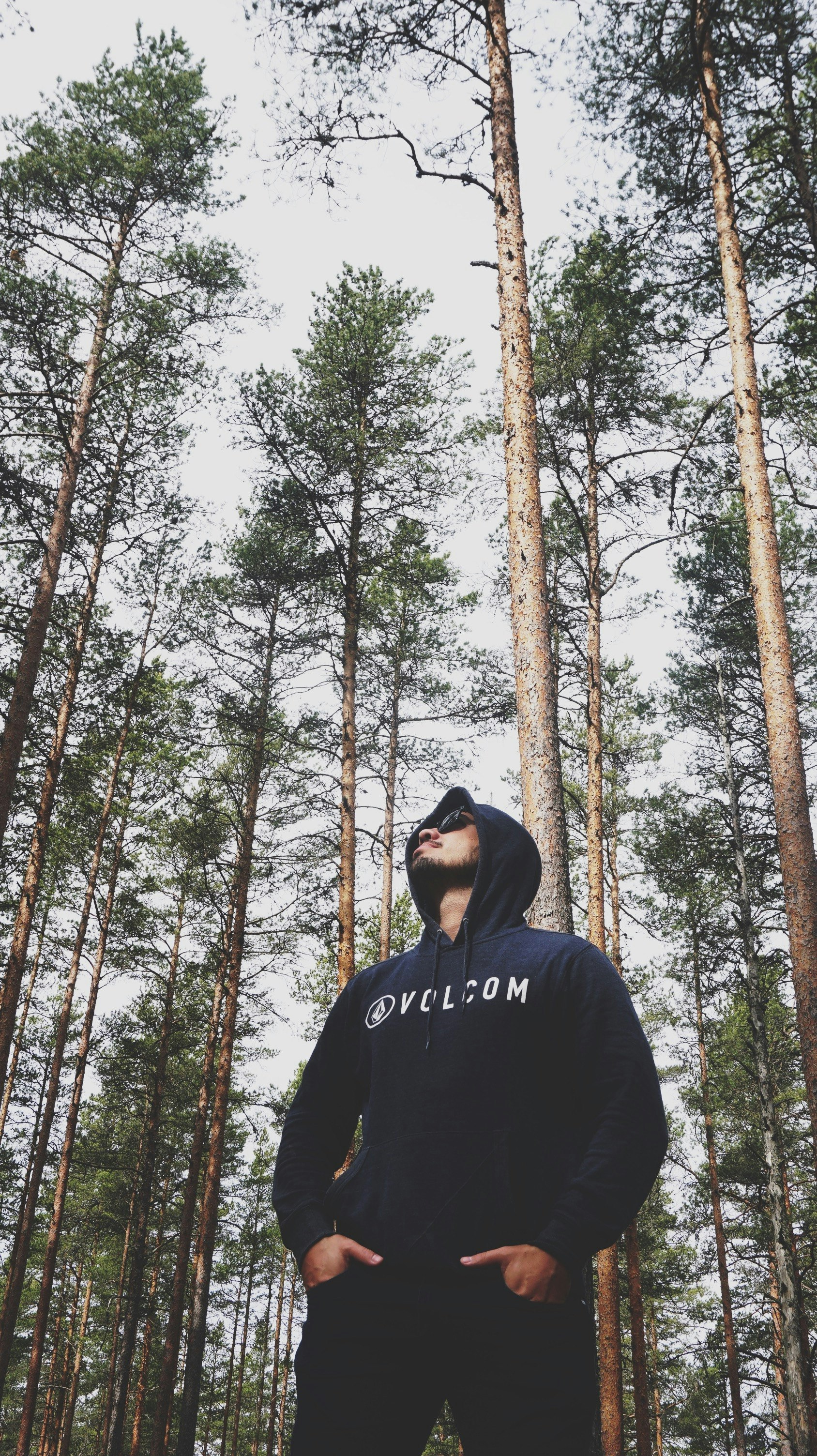 man in black hoodie standing in front of brown trees during daytime