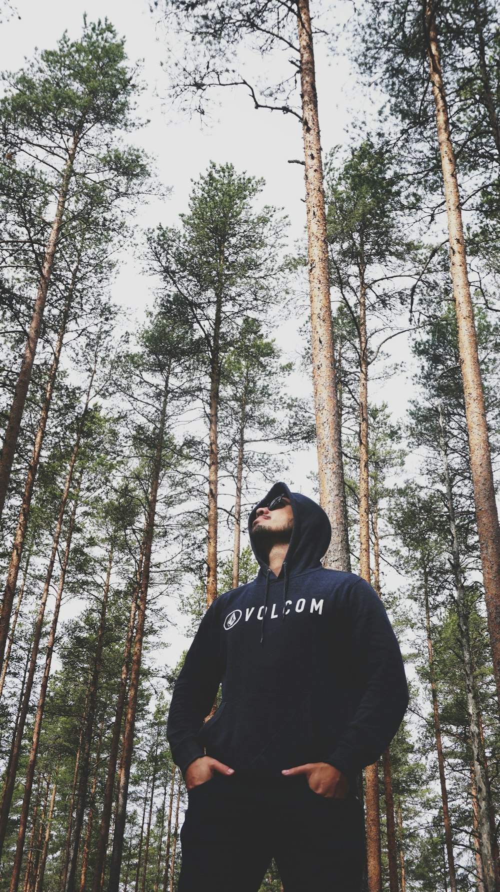 man in black hoodie standing in front of brown trees during daytime