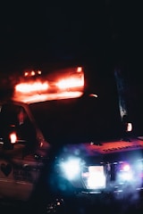 An ambulance with emergency lights flashing is visible in a dark setting. The vehicle is branded with 'Denver Health' on the side and the lights create a strong contrast against the darkness.