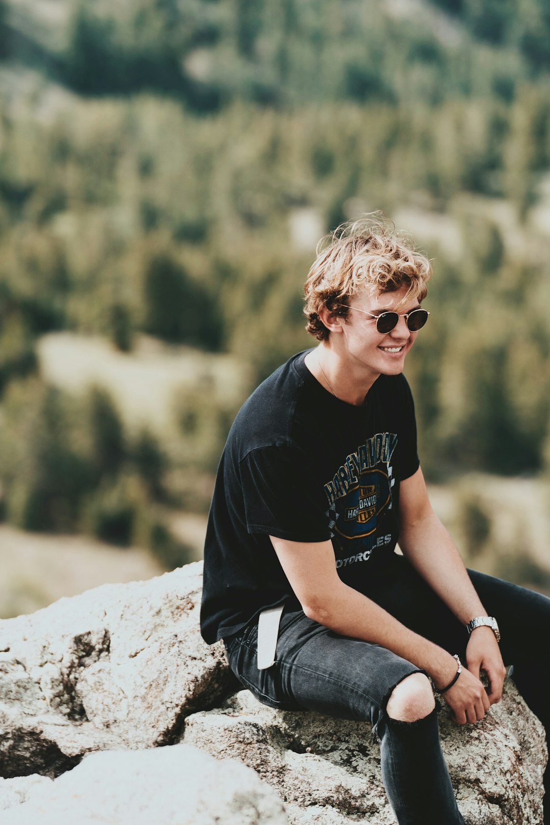 man in black crew neck t-shirt and gray denim jeans sitting on rock during daytime