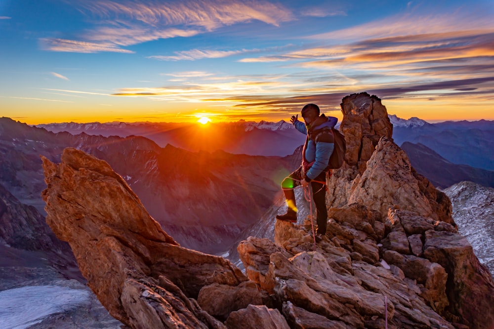 man in green jacket standing on rock formation during sunset