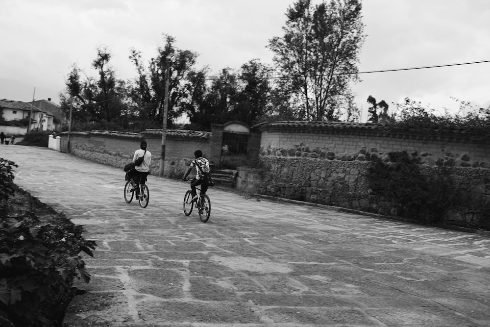 grayscale photo of 2 men riding bicycle on road