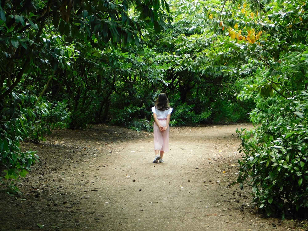 girl in white tank top and pink shorts walking on dirt road during daytime