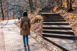 woman in brown coat and blue denim jeans walking on wooden bridge during daytime