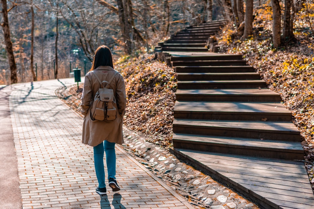donna in cappotto marrone e jeans blu denim che cammina sul ponte di legno durante il giorno