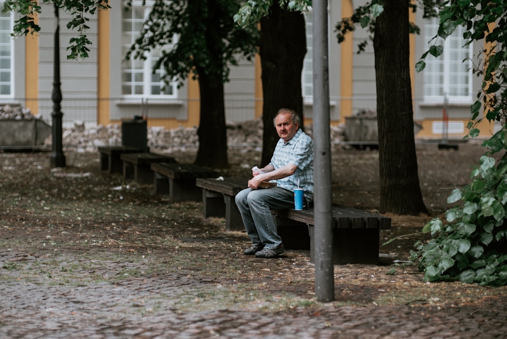 man in blue dress shirt sitting on brown wooden bench during daytime