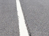 Close-up of smooth asphalt surface with road markings being painted.