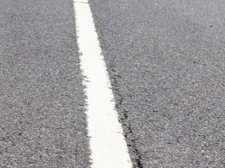 A close-up of a freshly sealcoated asphalt driveway with crisp white line striping under a clear sky.