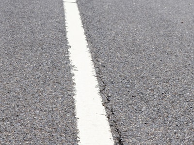 A close-up view of a textured asphalt road with a single white line running through the center.