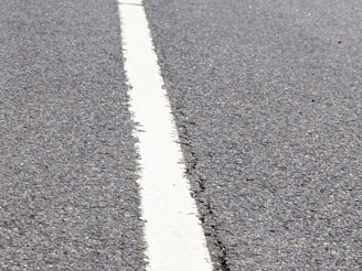 A close-up view of a textured asphalt road with a single white line running through the center.