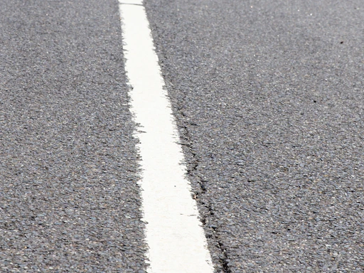 Close-up of fresh white road marking paint being applied on asphalt.