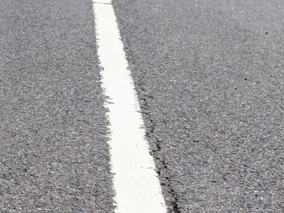 Close-up of smooth asphalt surface with road markings being painted.