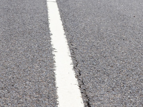 A close-up view of a textured asphalt road with a single white line running through the center.