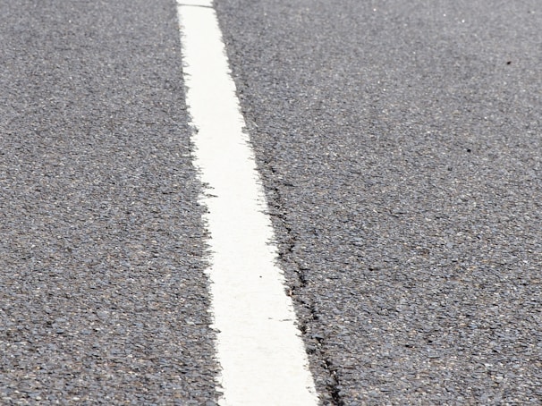 A close-up view of a textured asphalt road with a single white line running through the center.