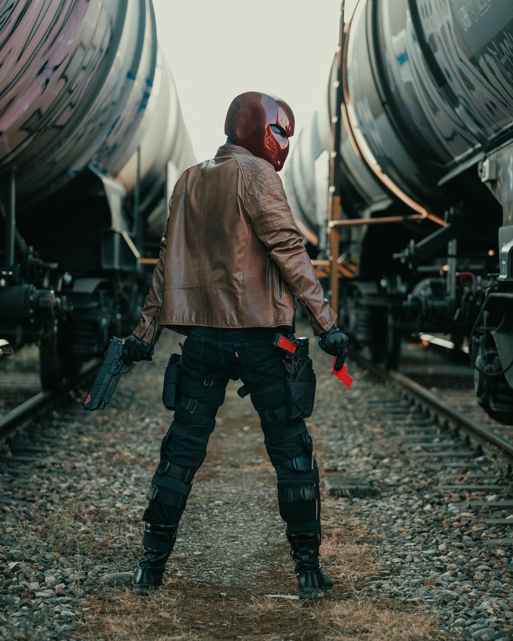 man in brown jacket and black pants standing on train rail during daytime