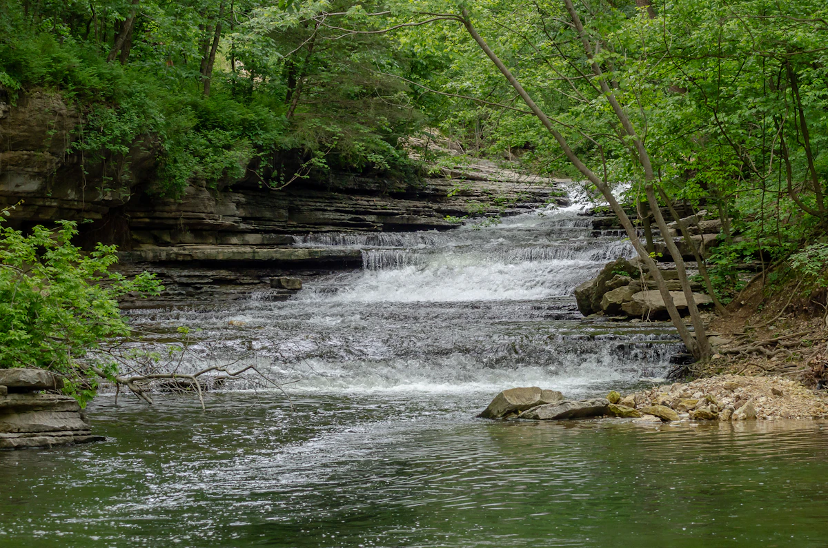 A tiered waterfall spilling over rock ledges on Tanyard Creek in Bella Vista, under green trees
