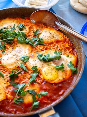Shakshuka with eggs nestled in a vibrant red tomato and pepper sauce topped with fresh cilantro and crumbled feta in a cast iron skillet