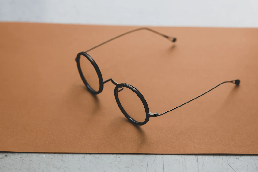 Runde schwarze Brille auf einem terrakottafarbenen Papierbogen in hellem Tageslicht