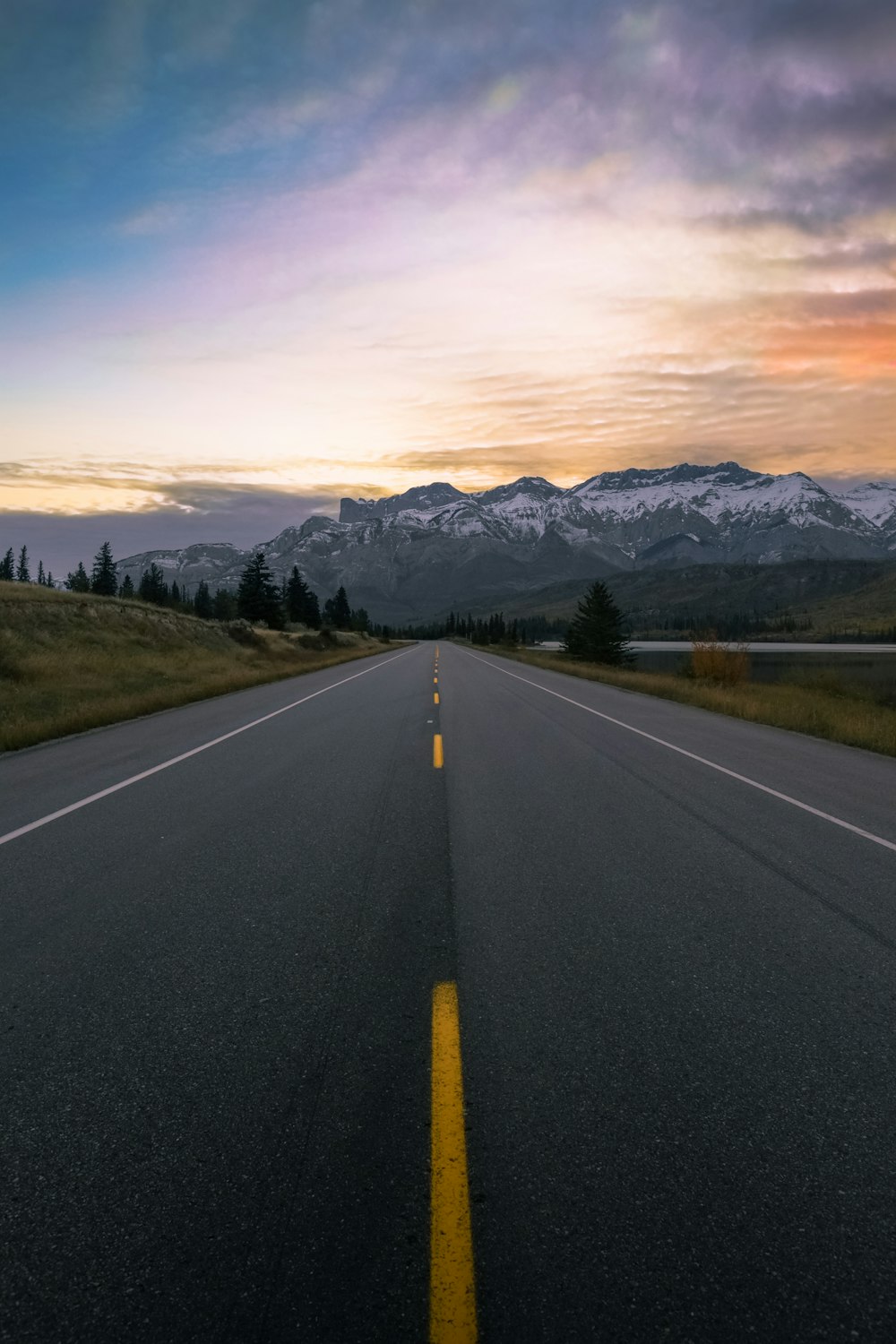 gray concrete road near green trees and mountains during daytime