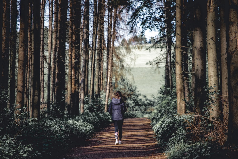 woman in black jacket walking on pathway between trees during daytime