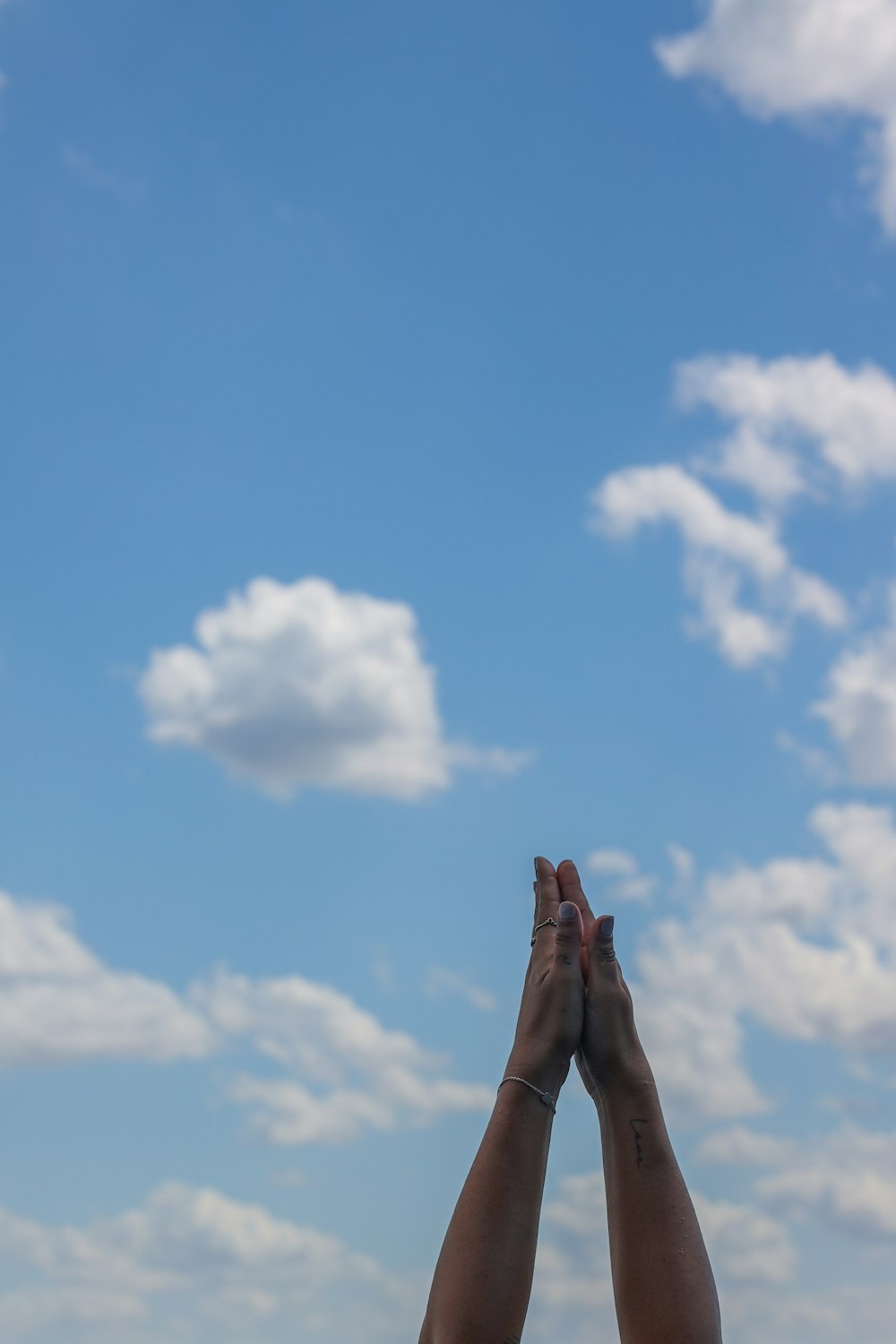 person raising his right hand under blue sky and white clouds during daytime