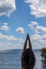 person raising his right hand near body of water during daytime