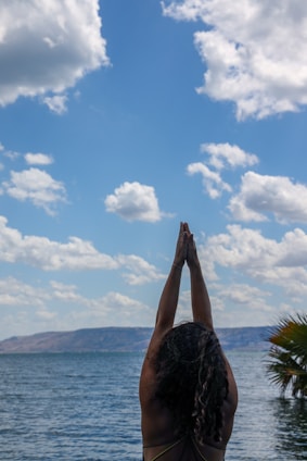 person raising his right hand near body of water during daytime