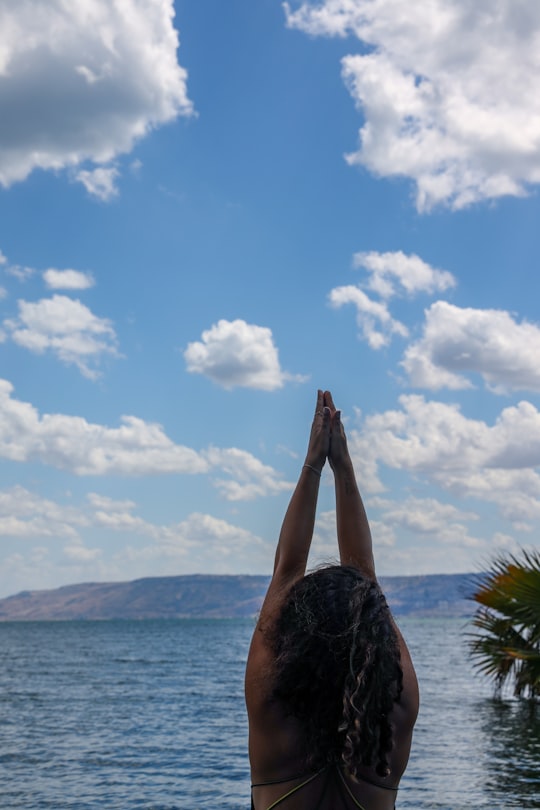 person raising his right hand near body of water during daytime in Sea of Galilee Israel
