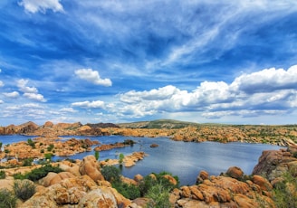 brown rocks on body of water under blue sky and white clouds during daytime