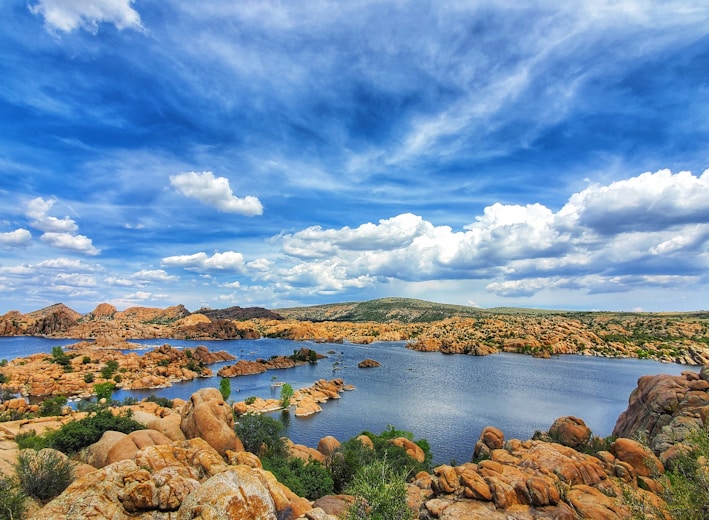 brown rocks on body of water under blue sky and white clouds during daytime