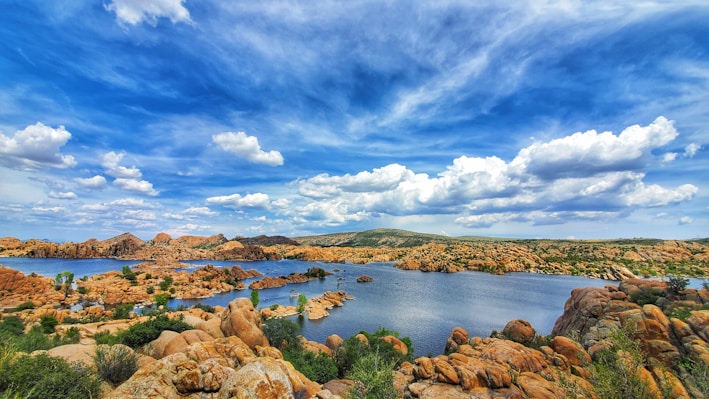 brown rocks on body of water under blue sky and white clouds during daytime