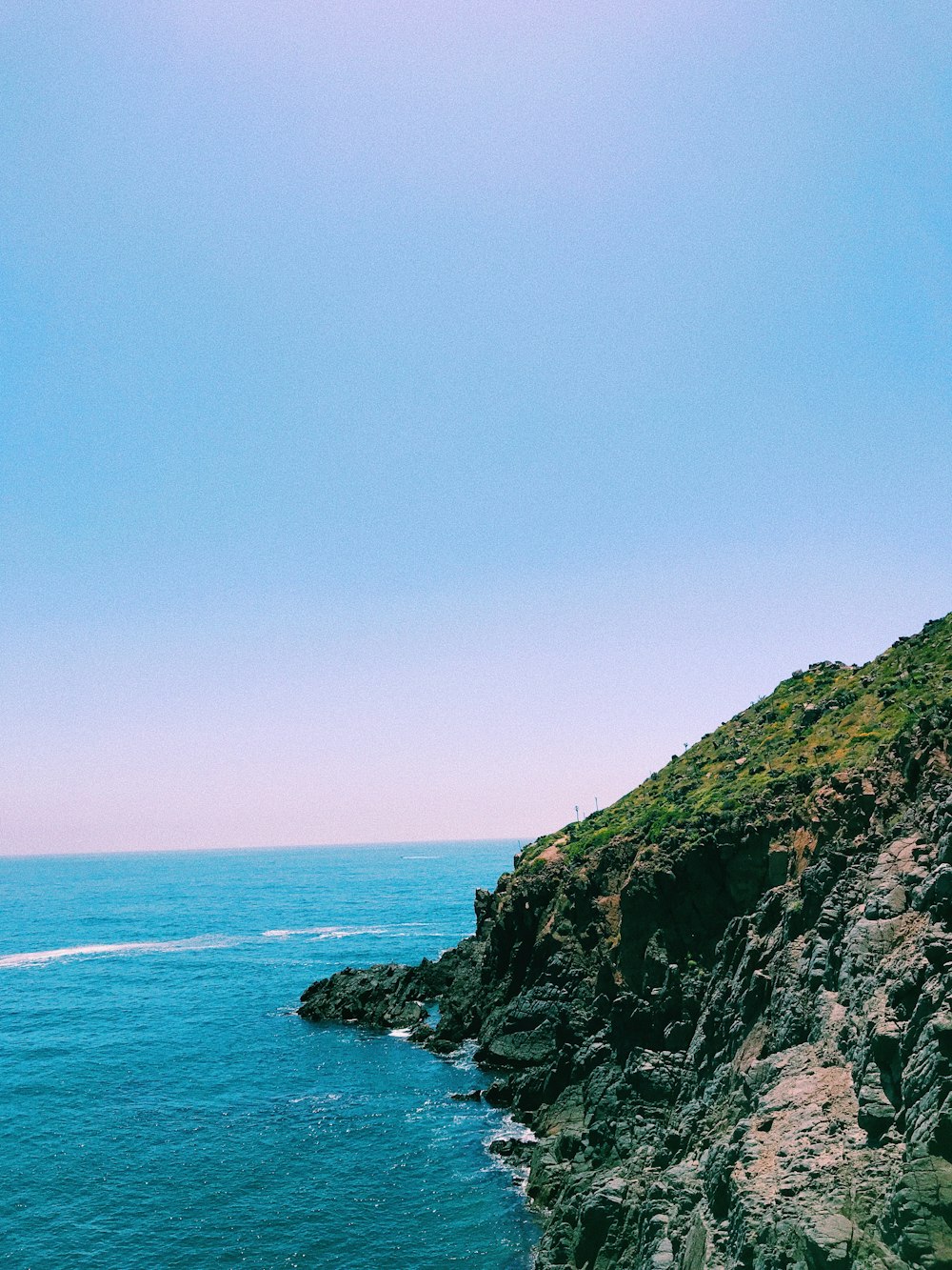 green and brown mountain beside blue sea under blue sky during daytime