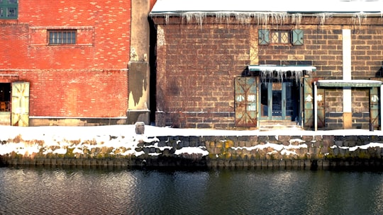 brown brick building near river during daytime in Otaru Canal Japan