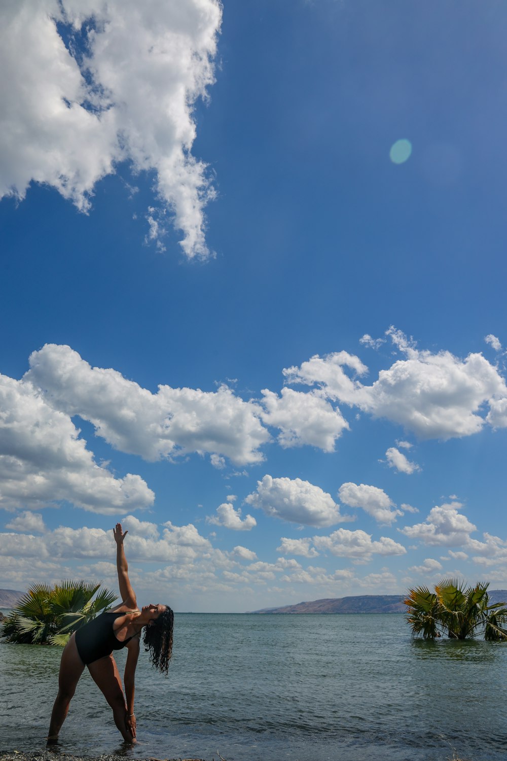 woman in black bikini standing on green grass field under blue and white cloudy sky during