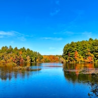 A clear lake reflecting autumn trees with vibrant orange and red leaves.