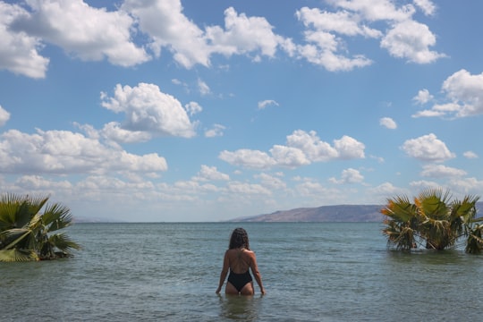 woman in black bikini sitting on beach during daytime in Sea of Galilee Israel