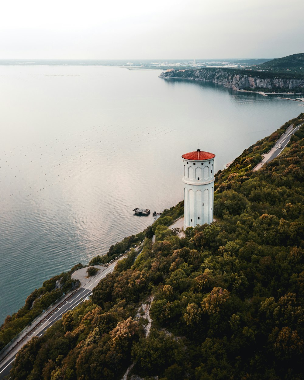 white and red lighthouse on brown and green grass field beside body of water during daytime