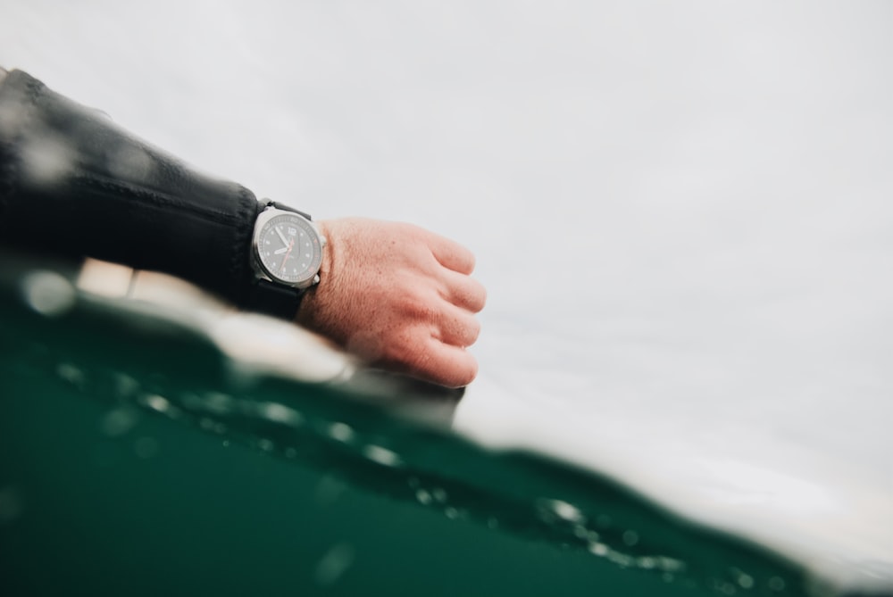 person wearing silver round analog watch with black leather strap