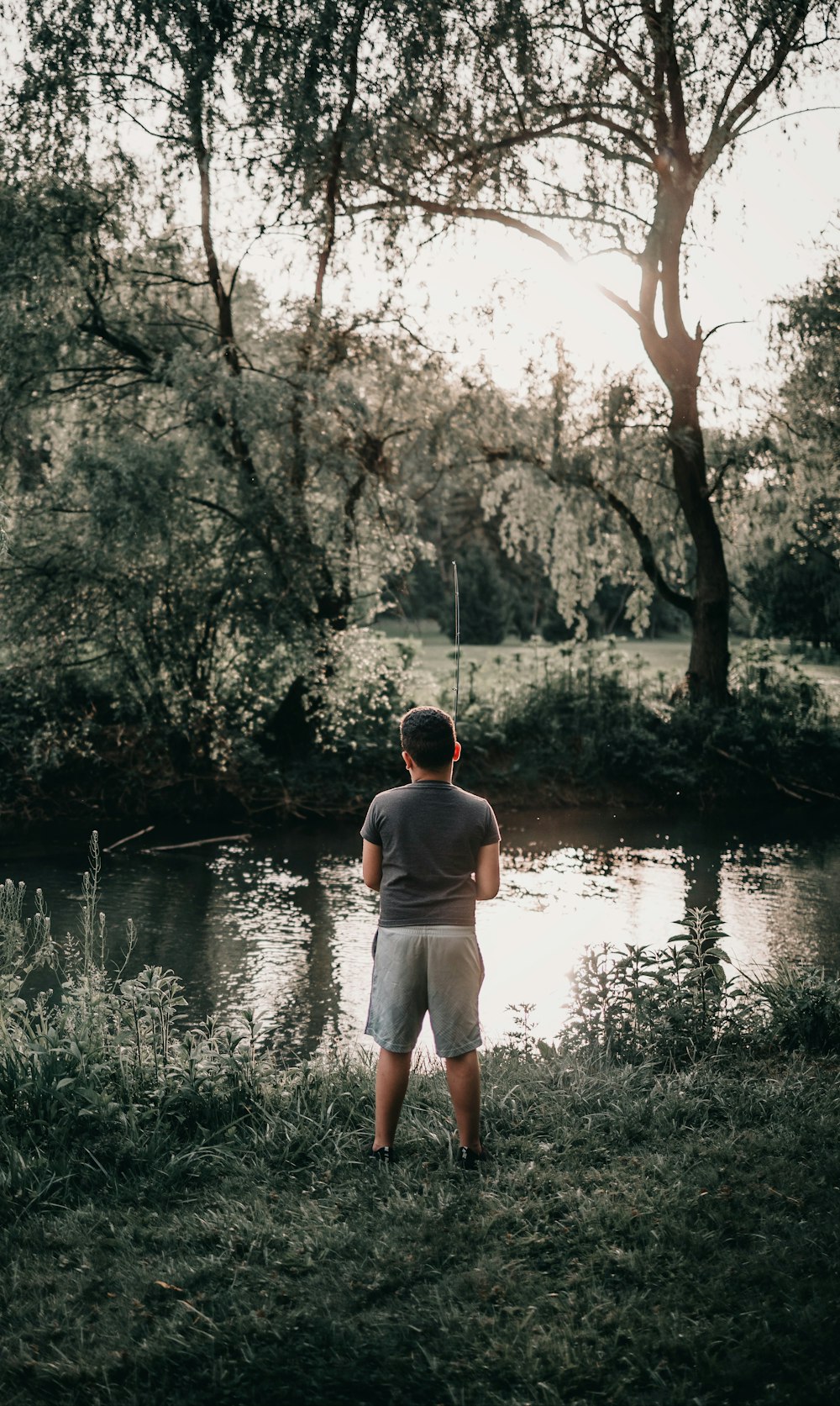 man in white tank top and white shorts standing on green grass field near lake during