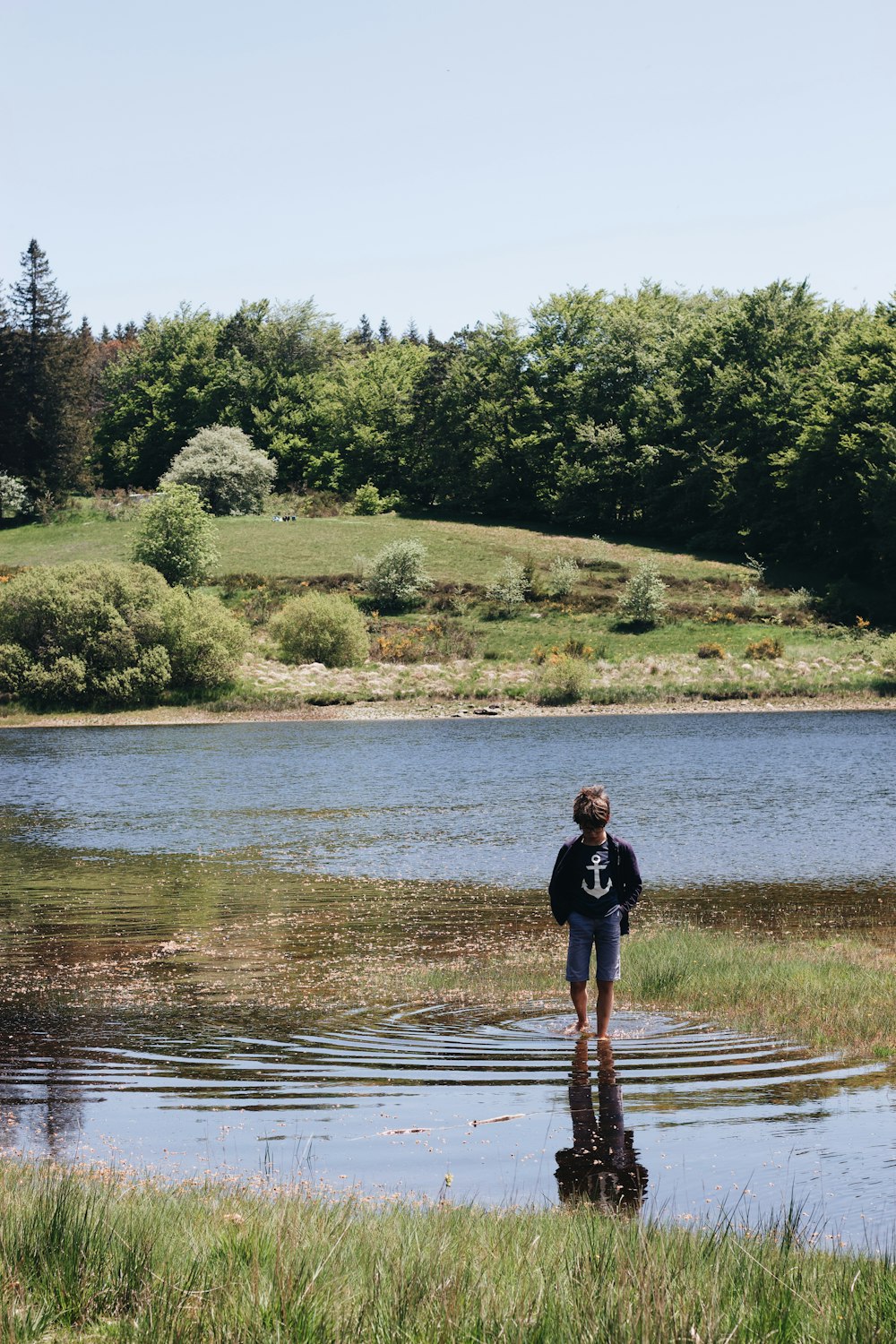 woman in black shirt standing on brown field near lake during daytime