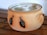 A ceramic pot with two handles and a lid, decorated with painted images of black birds. The pot is placed on a wooden surface and has a natural earthy color.