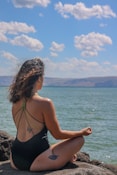 woman in black bikini sitting on rock near sea during daytime