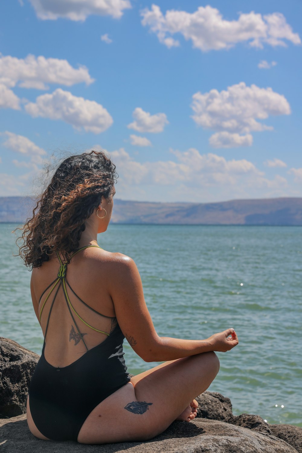 mulher no biquíni preto sentado na rocha perto do mar durante o dia