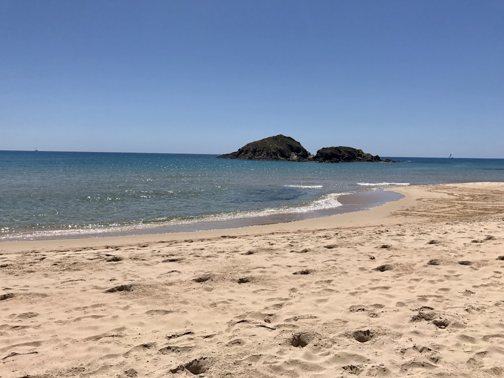 Plage de sable brun avec de l’eau bleue de l’océan sous le ciel bleu pendant la journée