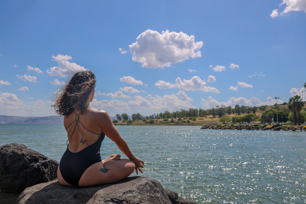 woman in black bikini sitting on rock near body of water during daytime