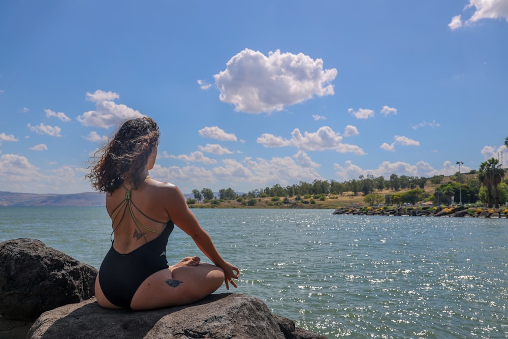 Mujer en bikini negro sentada en la roca cerca del cuerpo de agua durante el día