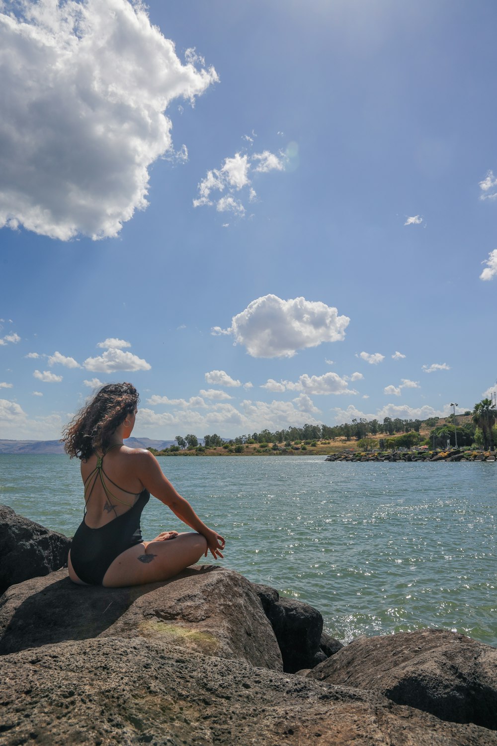 Frau im schwarzen Bikini sitzt tagsüber auf Felsen in der Nähe eines Gewässers
